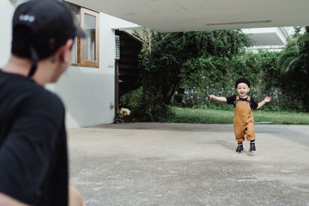 boy in dungarees running to his father outside the house